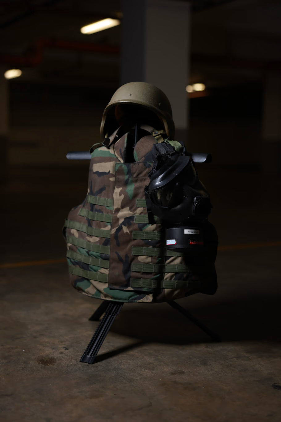 Camouflage vest and helmet on a Swift Portable Gearstand in a dark indoor setting.