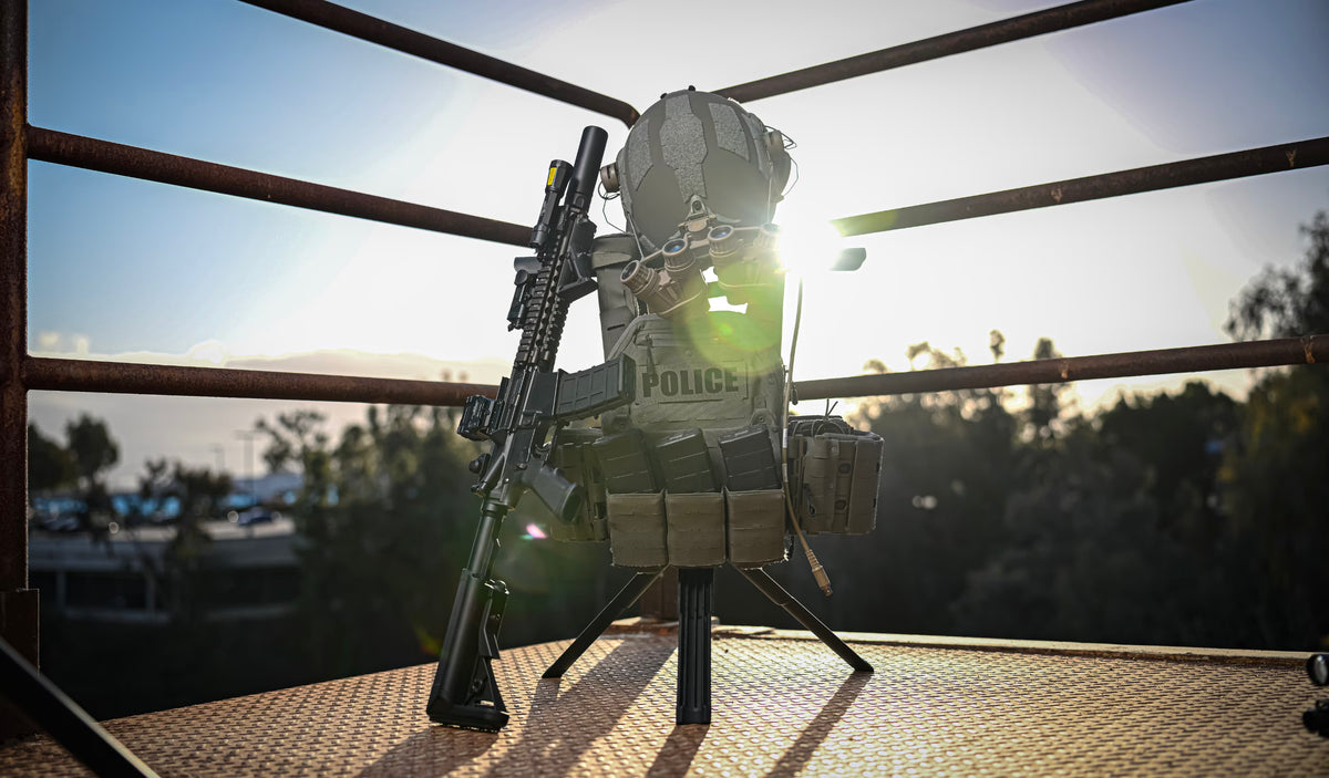 Swift portable gearstand supporting body armor and helmet with rifle leaning upright against it.  In the background is a railing and behind that the sunset.